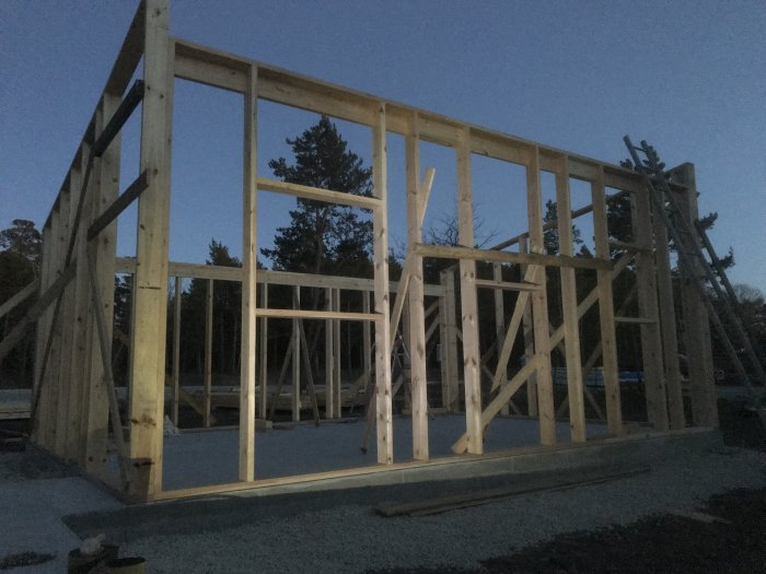 Delvis uppförd trästomme i skymningen med stödsträvor på betongplatta.