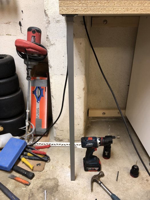 Verktyg och stödben monterade i ett garage, inklusive slagborr och olika chuckar på golvet.
