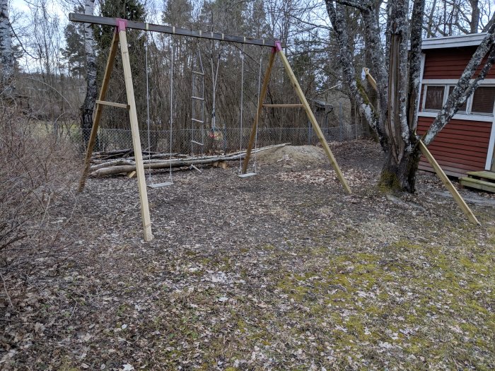 Gungställning i skuggig hörna av trädgården med löv på marken och buskar i bakgrunden.