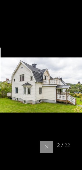 Vit villa med svart tak och tre stora fönster på vänster sida, grönt gräs framför.