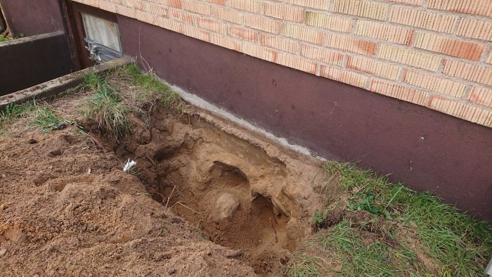 Erosionsskador nära grund av hus, synlig sättning och fuktspår på betongfundamentet.