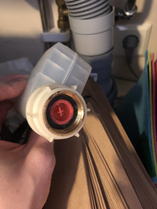 Närbild på en hand som håller en demonterad vit plastdel med en röd stjärna och svart packning.