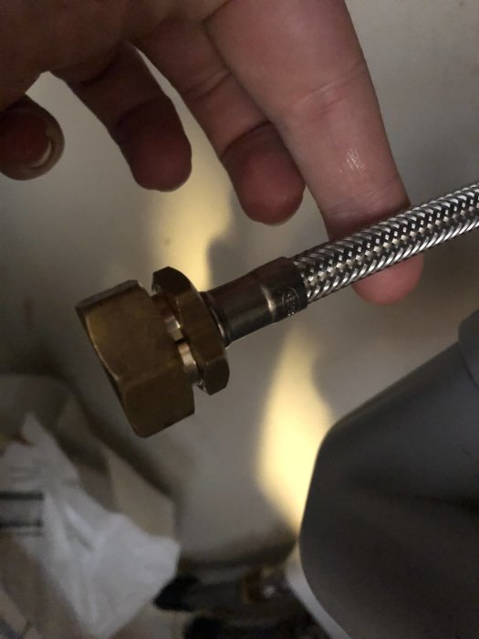 Hand håller en flexibel vattenslang i metall med mässingskoppling.