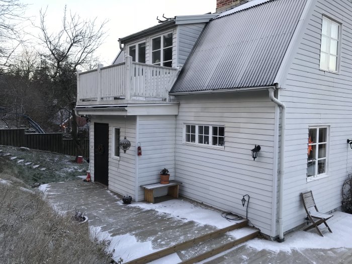 Vitmålad 20-talsvilla med en liten yttre hall och en balkong ovanpå, omgiven av snötäckt mark och vinterlandskap.