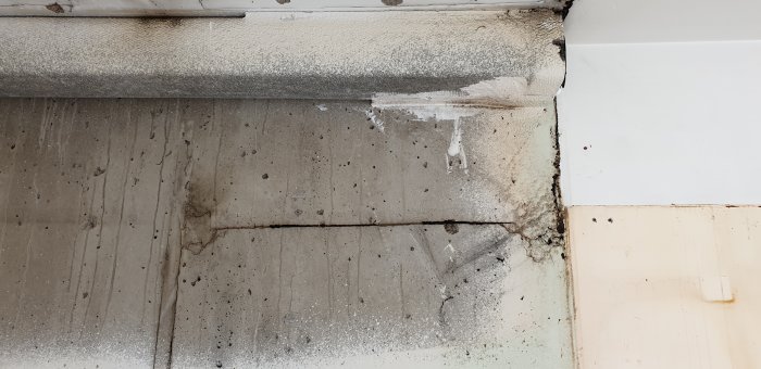 Slitet hörn i ett rum med synlig skarv mellan betongplattor, damm och möjlig asbestförorening vid renovering.