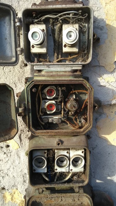 Gammal elektrisk installation med öppna kopplingslådor och synliga, slitna ledningar på en vägg.