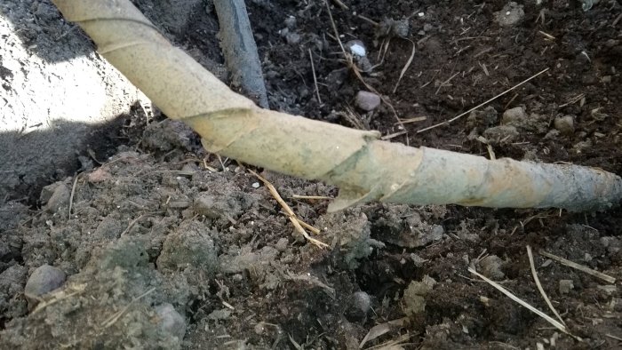 Skadad elledning med av stålband och synlig korrosion, delvis begravd i marken.