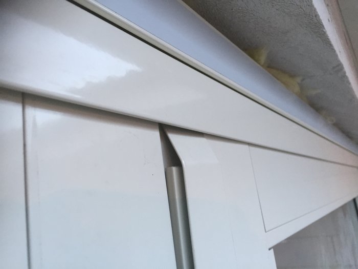 Närplan av en vit skjutdörr med böjd aluminiumbeklädnad längs övre kanten, relevant för diskussion om installation.