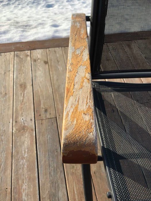 Slitet träarmstöd på utemöbel med flagnande lack och svarta fläckar, på en terrass med snö i bakgrunden.