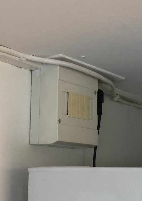 Gammal vit väggmonterad elapparat med lucka och svart kabel i ett kök från 60-talet.