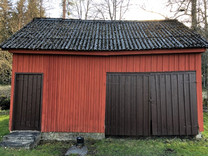 Rödmålad träuthus med svart eternittak och dubbla bruna dörrar, som ska omvandlas till gästhus.