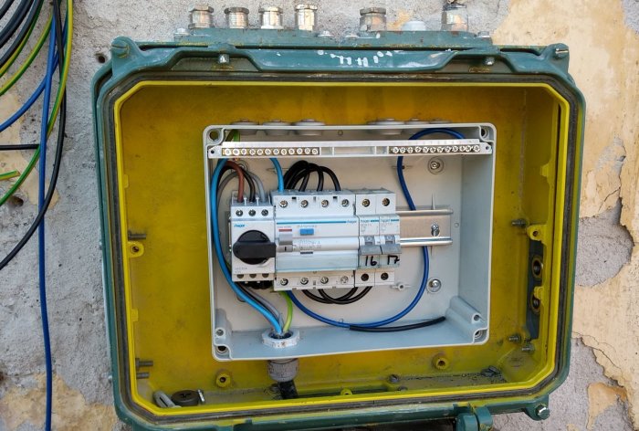 Öppen gul Spelsberg AK12 normkapsling monterad i en stor grön låda, med kablar och elektriska komponenter installerade.