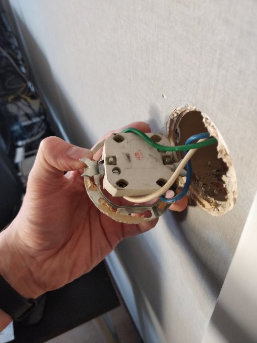 Hand håller en öppnad strömbrytare med vajrar inne i en vägg för att ändra belysningskoppling.