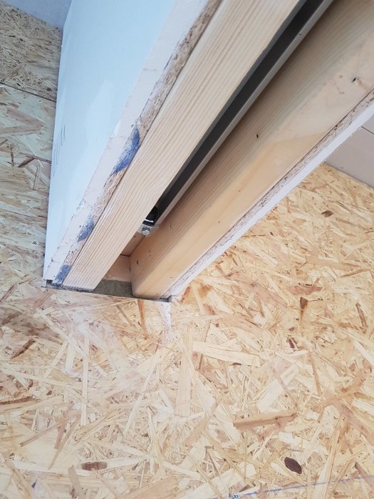 Detaljvy av vägg med skjutdörr och reglar, osb-skiva och gips synliga, behov av avslut mot dörrhålet.