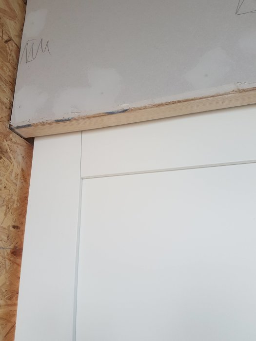 Vägg under konstruktion med synliga OSB och gipsskivor ovanför en skjutdörr.