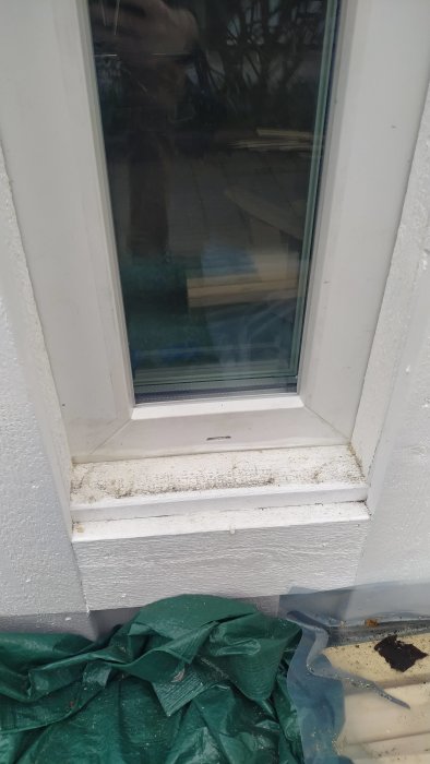 Fönster med utvändigt monterat och målat foder utan fönsterbleck, nära marken.