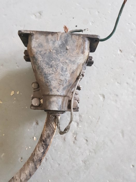 Gamla elektriska muffen med öppna sladdändar och en metallklamma fixerad mot betonggolv.