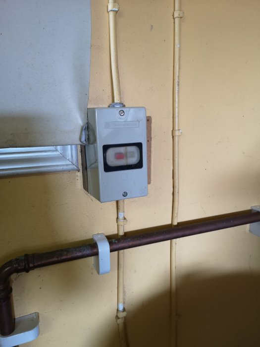 En väggmonterad elektrisk brytare med tillhörande rörinstallation i ett garage.
