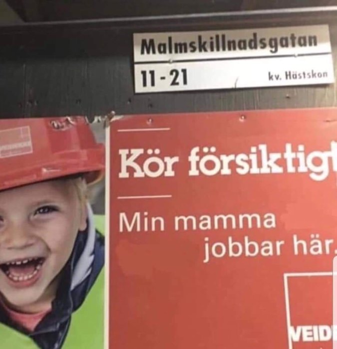 Skylt med texten "Kör försiktigt, Min mamma jobbar här" under en gatuskylt som visar "Malmskillnadsgatan".