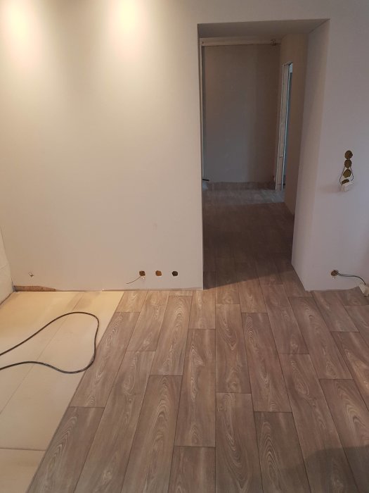 Nyinstallerat laminatgolv och orörda lister längs väggar i ett tomt rum i renoveringsfas.