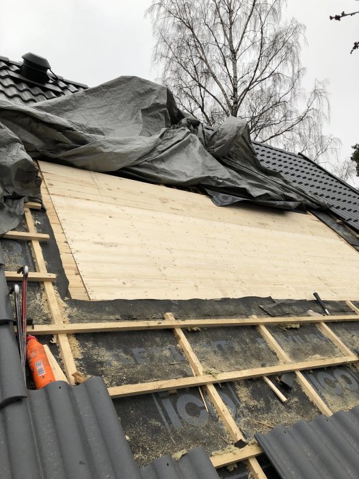 Renoverat takparti med ny råspont och överlappande takpapp, i väntan på fönsterinstallation.