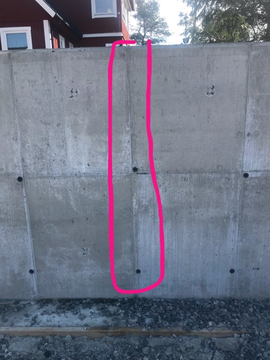 Nybyggd betongmur med tre markerade sprickor på en obebyggd tomt.