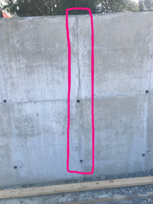 Nybyggd grå mur med markerade stora sprickor och synliga gjutformshål på en byggarbetsplats.