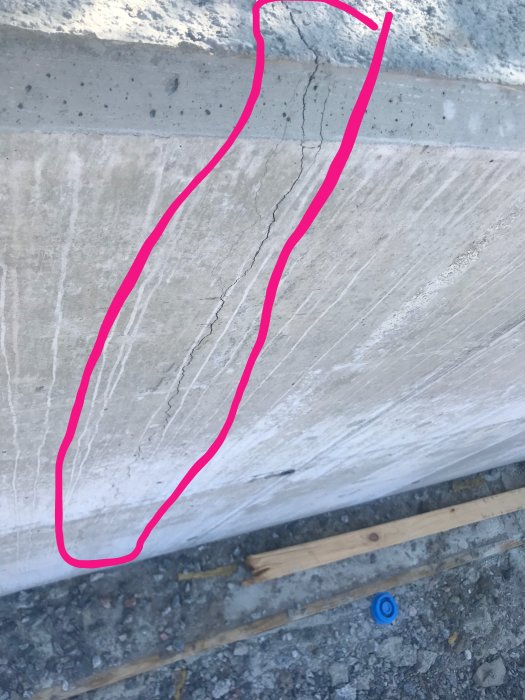 Nyligen byggd betongmur med markerade stora sprickor och grusig mark i förgrunden.