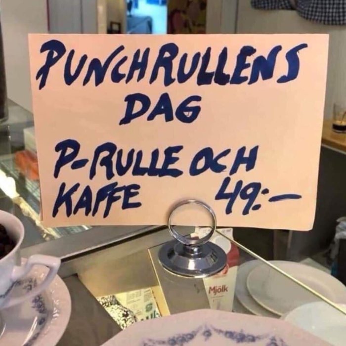 Skylt med texten "PUNCHRULLENS DAG P-RULLE OCH KAFFE 49:-" framför disken i ett café.