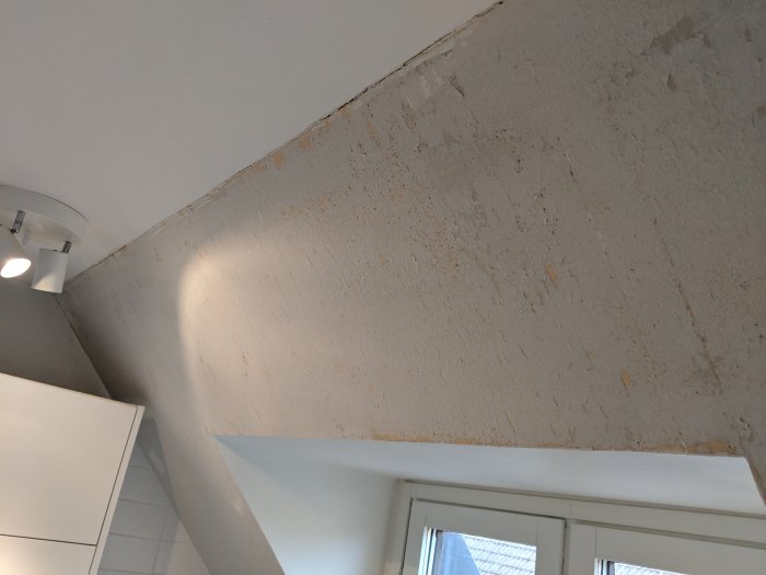 Kök med snedtak och ojämn vägg där gammal strukturtapet har rivits ner, med synliga skarvar och spackelrester.