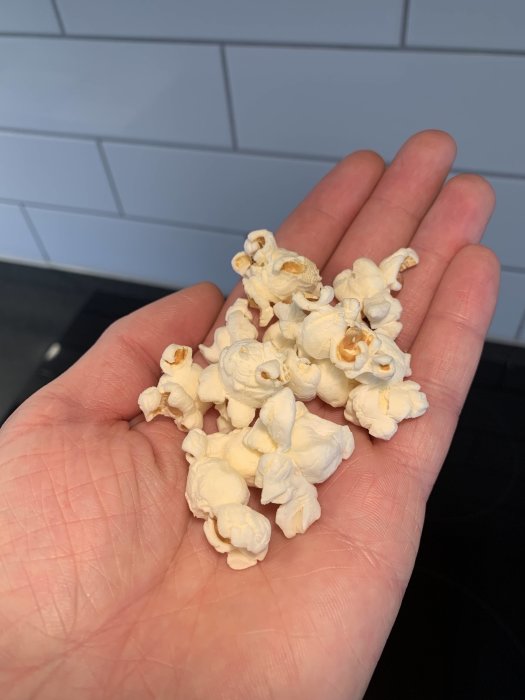 En hand håller nygjorda popcorn poppade i mikro med en speciell metod.