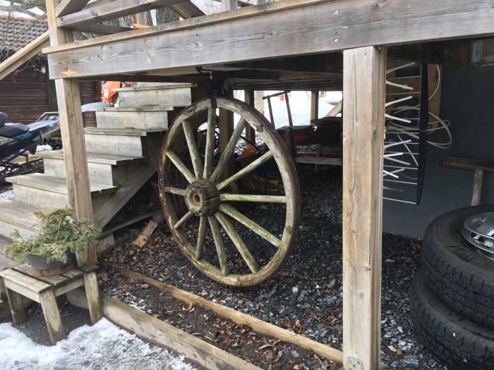 Två upphängda begagnade sommardäck under en träkonstruktion med snörester och trädäck i bakgrunden.