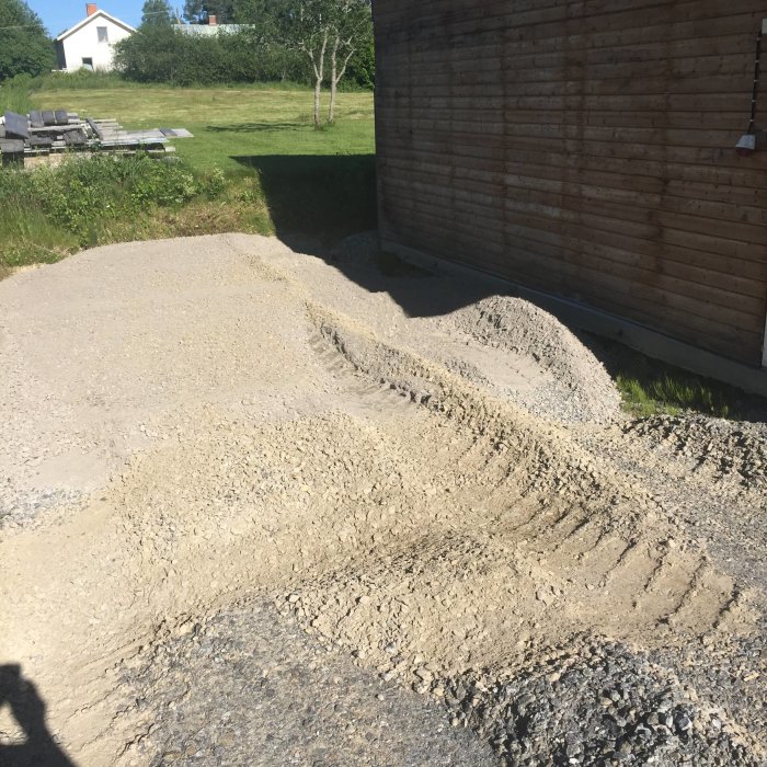 Grävmaskinsarbete vid garage med grushög och utgrävd mark inför byggande av förråd.