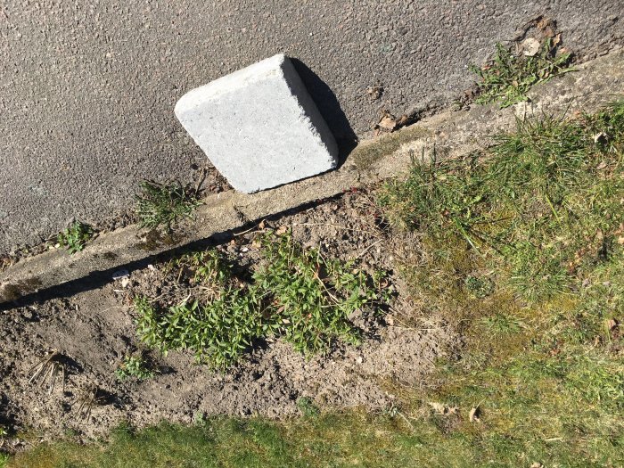 En trottoarkant med trasig asfalt och en vit trottoarprisma liggande på sidan.