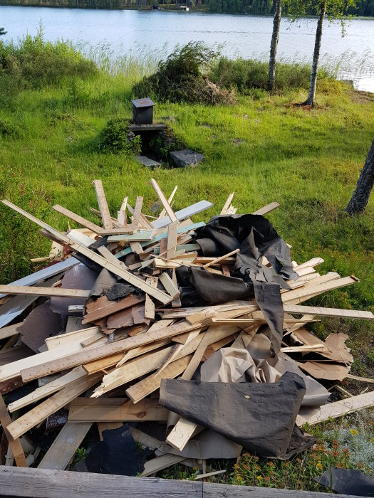 Hög med förstört trämaterial och annat byggavfall framför sjö och natur, skador av hästmyror.