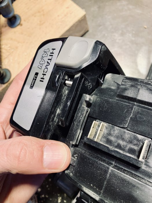 Närbild på ett Hitachi batterifäste som hålls i en hand, synlig slitage och damm på plasten.