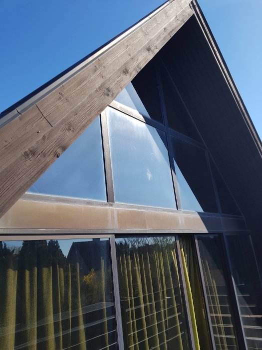Vinklad vy av en husvägg med stora fönster upp till taknocken under en klarblå himmel.