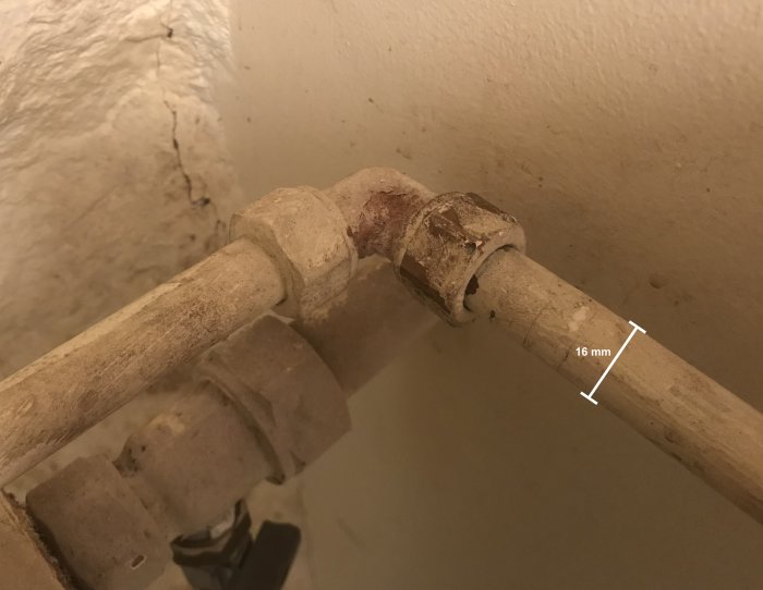 Gammalt 16mm rör i källare med målad yta och rost nära en vinkelkoppling som behöver proppas igen.