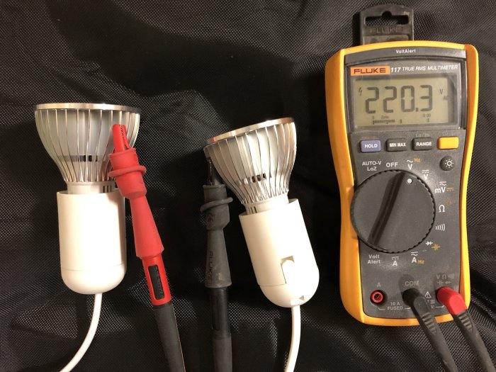 Spänning mäts på två LED-växtlampor med multimeter som visar 220.3V AC.