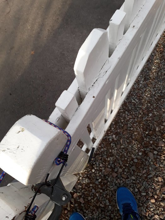 Närbild på en vitmålad grind med sprickor i färgen och detaljerade träpinnar, sett ovanifrån mot en grusgång.