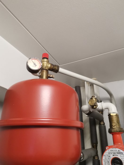 Röd expansionskärl till värmesystem med manometer och rörkopplingar.