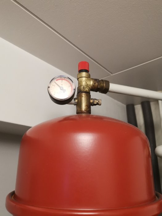 Röd expansionskärl med tryckmätare för värmesystem monterat på vit rörledning.