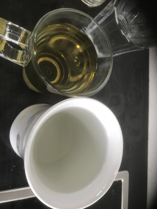 En genomskinlig mugg med gul vätska bredvid en vit mugg på en svart yta.