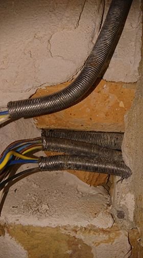 Elektriska rör och kablar som går in i ett hål i väggen, med synliga ledningar och betong.