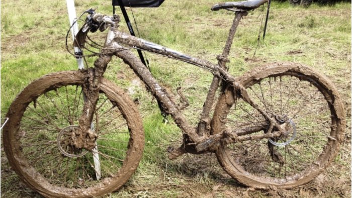 Mountainbike täckt i tjockt lager av lera, står på gräs.