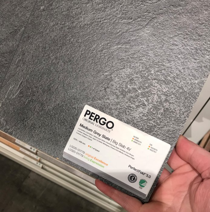 Hand håller ett varuprov för Pergo Original Laminatgolv i nyansen Medium Grey Slate.