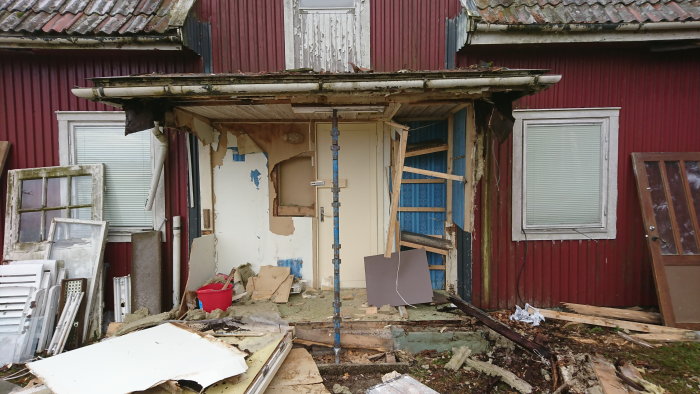 Försummat rött trähus med skadad fasad och bråte, under renovering med avlägsnade delar av väggar och tak.