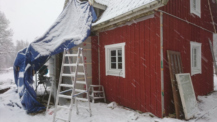 Renovering av husexteriör på vintern med stegar och snötäckt presenning.