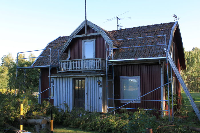 Ett gammalt hus med röda och vita fasader och takplåt under renovering med byggnadsställningar uppställda.