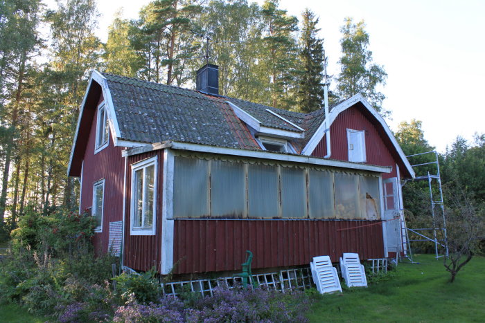 Ett rött trähus med takplåt och en pågående renovering, inklusive byggställningar och öppna väggpartier.